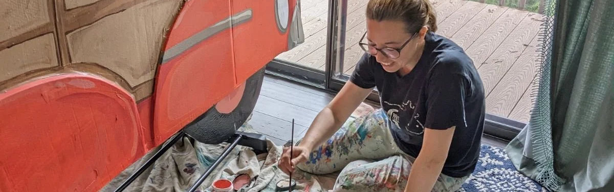 Amber Rankin painting a prop sitting on the floor.