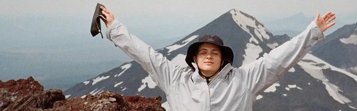 Lourdes Ginart Standing on top of mountain peak with arms above head.